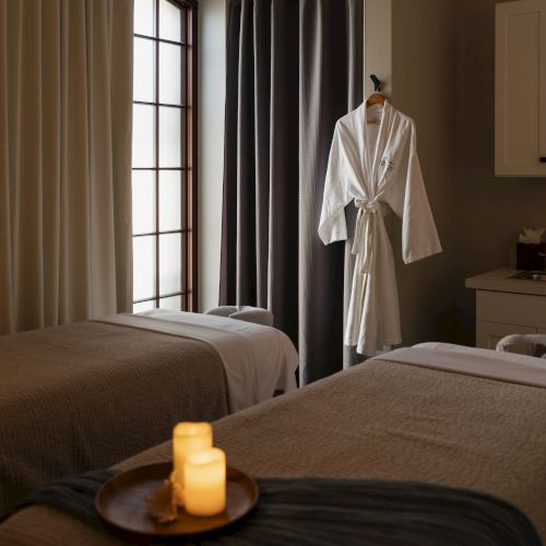 Two neatly made spa-like hotel rooms with soft lighting, candles on a tray, and a white robe hanging by a window and cabinets.