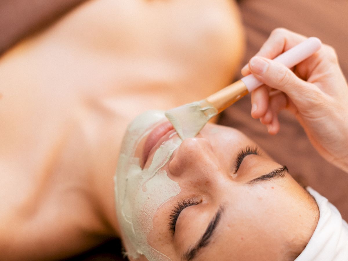 A person receiving a facial treatment, with a green facial mask being applied by a therapist. End.